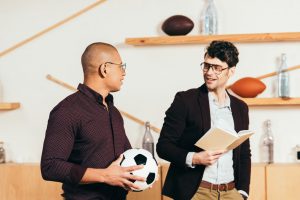 Football coach reading a book while friend holds a football